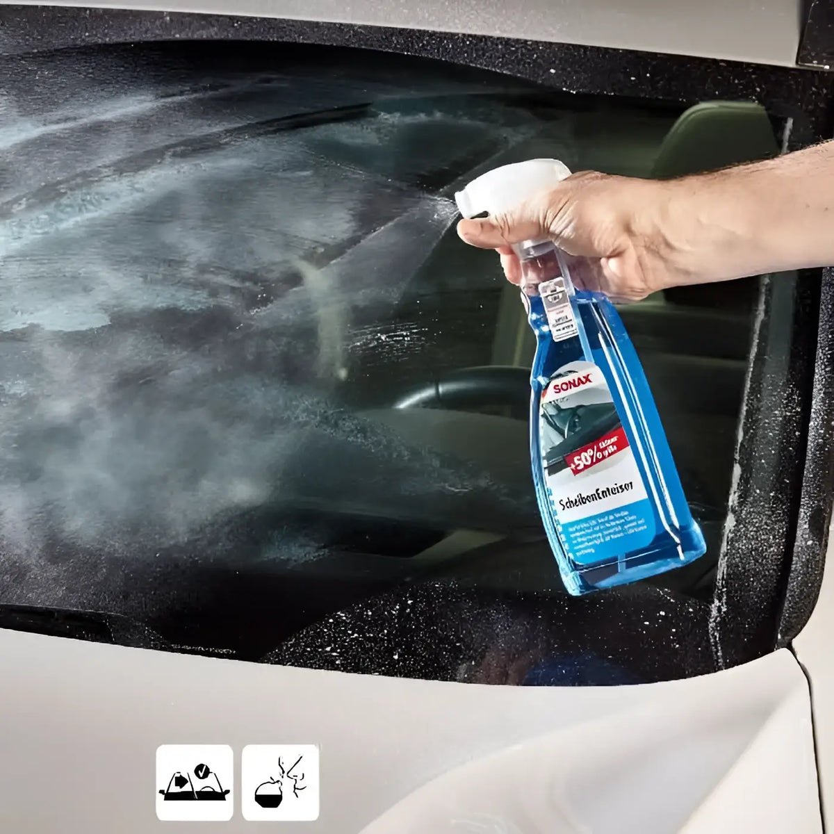 Blauer sonax scheibenenteiser spray mit weißer düse in hand über frostbedecktem autofenster