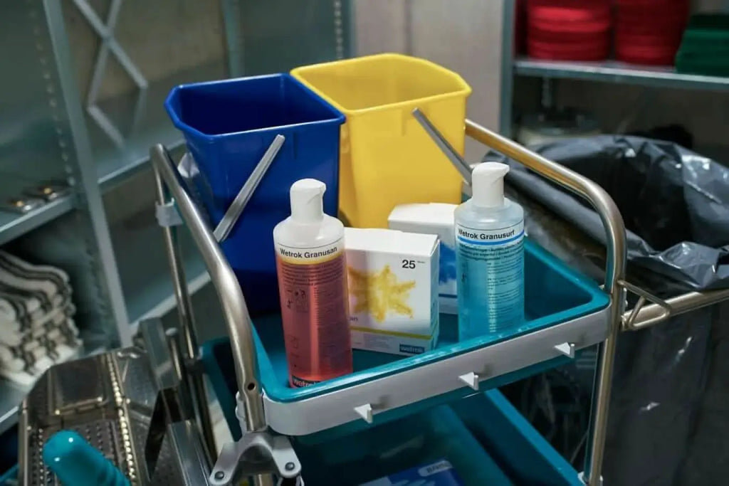 Blaue und gelbe plastik Eimer mit metallgriffen auf einem medizinkarren neben flaschen des wetrak granusan desinfektionsmittels